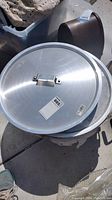 Top view of giant aluminum pot with lid resting on top, lid featuring handle and measurement tag visible.