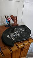 Photo of black lacquer tray with abalone and mother of pearl floral and butterfly inlay, placed on wooden furniture, with Black Americana figurines in background.