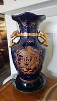 Front view of cobalt blue vase with gold ornamental details and elephant-shaped gold handles on white shelf.