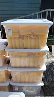 Three clear plastic tubs stacked vertically outdoors with yellow squeeze condiment bottles visible inside each tub.