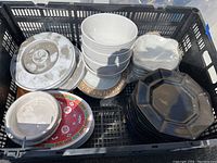 Top view of crate containing stacked white cereal bowls, red and white plastic plates, and small octagonal black plates.