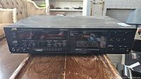 Front view of JVC stereo cassette deck showing control buttons, cassette compartment with tape inside, and level meters.