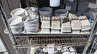 Shelved white porcelain ramekins and rectangular condiment dishes on a metal rack outdoors