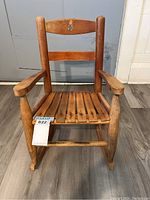 Front view of vintage child's wooden rocking chair showing the slatted seat, armrests, and painted decoration on top backrest.