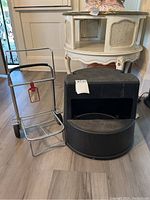Photo showing a metal luggage roller frame with two wheels and handle next to a black vinyl covered revolving step stool with curved base and open middle section.