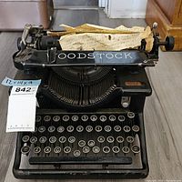 Front view of the vintage Woodstock typewriter showing the keyboard, paper carriage, and branding with a torn paper sheet inserted.