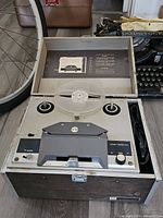 Front view of open Webcor reel to reel tape recorder showing the two reel spindles, control knobs, and instruction label on the inside of the lid.