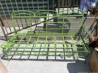 Green wrought-iron outdoor seater with backrest and one armrest detached, showing the frame structure and decorative elements