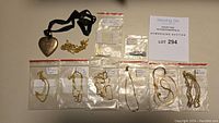 Overview of all jewelry items laid out: six zip-lock bags with gold chains and a heart locket on ribbon