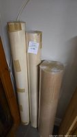 Three vertically standing rolls of heavy paper wrapped in plastic and tape.