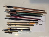 Overhead view of twelve dip pen holders and nibs arranged side by side on white background