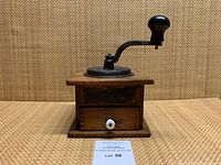 Front view of antique Imperial coffee grinder in wood with metal crank and drawer with white knob.