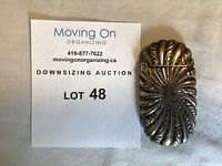 Photo of the sterling silver sunburst match case closed next to auction lot number card.