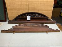 Pair of carved wooden architectural pieces on table, showing overall size and shape, straight-on view.