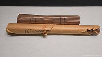 Two rolls of thin copper sheets wrapped in brown paper, one labeled 16 inches, placed horizontally on a white surface.