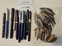 Ten fountain pens arranged beside a clear plastic bag of loose nibs