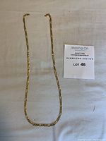 Full view of gold chain necklace laid flat on fabric beside lot number card