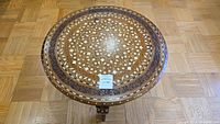 Top view of round wooden tabletop with intricate white floral geometric inlay pattern