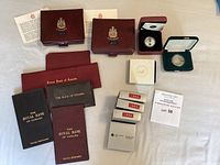 Overview of burgundy Royal Canadian Mint coin cases (1974, 1975), bank passbooks, grey-labelled coin boxes and white 1987 loonie box