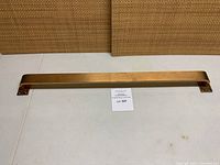Solid bronze commercial door pull laid flat on white surface showing full length handle and mounting plates