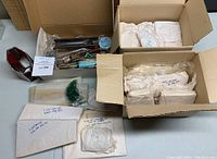 Overall lot displayed: two boxes containing various stained glass pieces wrapped in paper, 5 caramel slag glass sheets, small green glass pieces in plastic bag, and metal smouldering iron tool in original tray with cords.