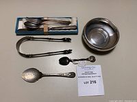 Overview of box with cutlery, loose utensils, sugar tongs, small spoon, sugar server spoon, and Birks bowl
