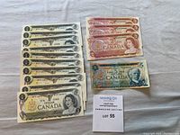 Twelve 1973 one-dollar bills, three 1974 two-dollar bills, and one 1972 five-dollar bill arranged on a cloth surface with auction lot card.