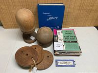 Overview of two wood hat blocks, four wooden spacer stands, stack of millinery manuals and packaged hat pins