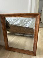 Front view showing wood frame and mirror reflecting bed and floor, minor marks visible on glass and slight scuffs on frame.