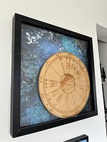 Close-up angle showing the framed astrological wheel mounted on a wall with visible zodiac signs, divisions, and astrological symbols drawn on a wooden wheel.
