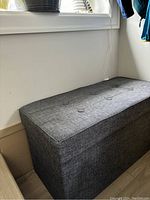Side angle view of grey fabric storage bench showing textured upholstery and button tufting on top
