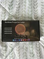 Photo of the box packaging of the rainbow projector lamp showing product image and features.