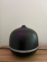 Front view of the black dome-shaped essential oil diffuser showing textured surface and white base strip.