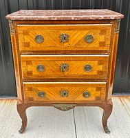 Front view of three-drawer marquetry commode with red marble top, ormolu circular pulls, keyhole escutcheons and cabriole legs