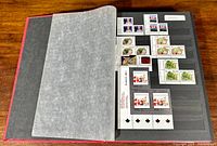 Photo showing open album page containing unused Canadian postage stamps from 1992, includes stamps with images of Queen Elizabeth, Canadian flag, flora, and art.