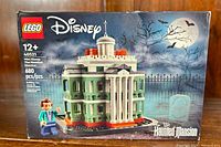 Front view of sealed LEGO Disney Mini Haunted Mansion box with model image, bat and moon background, showing set number 40521, piece count 680, and age recommendation 12+. Includes minifigure image on box.