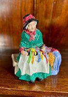 Front angled view of the Royal Doulton Silks & Ribbons figurine showing detailed coloring and ribbons on lap and side bench.