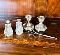All five items displayed together on wood surface: two cut crystal shakers with silver tops, two silver candlesticks, and two silver swizzle sticks.
