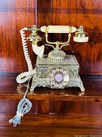Front view of ornate gold-tone rotary dial telephone