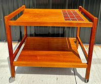 Front three-quarter view of the two-tier teak bar cart showing tile inlay and casters