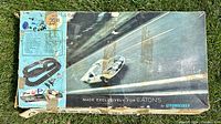Original Strombecker slot car set box photographed outdoors on grass, showing entire box top with racing car artwork and Eaton's branding. Tape and wear visible.