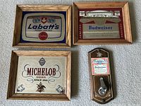 Top view showing three beer brand framed bar mirrors (Labatt's, Budweiser, Michelob) and one Budweiser wall-mounted bottle opener on wood plaque, arranged on flat surface.