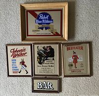 Photo showing five bar-themed bar mirrors laid out on a carpeted surface. Includes branded mirrors for Pabst Blue Ribbon beer, Johnnie Walker Scotch whisky, Dunhill snuff, and Beefeater gin, plus a smaller 'BAR' text mirror.