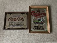 Photo showing two framed bar mirrors, one promoting Carlsberg Beer, the other Coca-Cola, placed on a floor against a wall.
