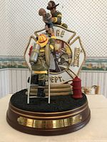 Front view of the firefighter figurine showing the child rescue scene in front of a Maltese cross emblem on a round wooden base with nameplate.