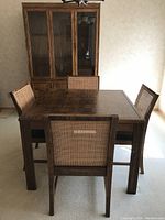Full view of the oak parquet dining table with four chairs and one-piece hutch in background
