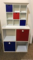 9-square white display shelf with three removable fabric boxes in red and blue pocketed into white compartments.