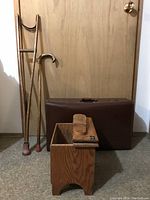 Photo showing entire lot: wooden crutch, cane, shoe shine box, and closed brown suitcase