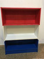 Front view of three-tier bookshelf with red, white and blue shelves.