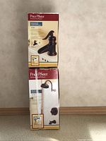 Two stacked boxes showing Price Pfister bathroom faucet and shower sets in rustic bronze finish.